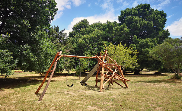Um elemento de playground feito de madeira; árvores podem ser vistas ao fundo.