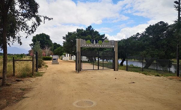 The entrance gate on an unpaved road can be seen; a river to the right.