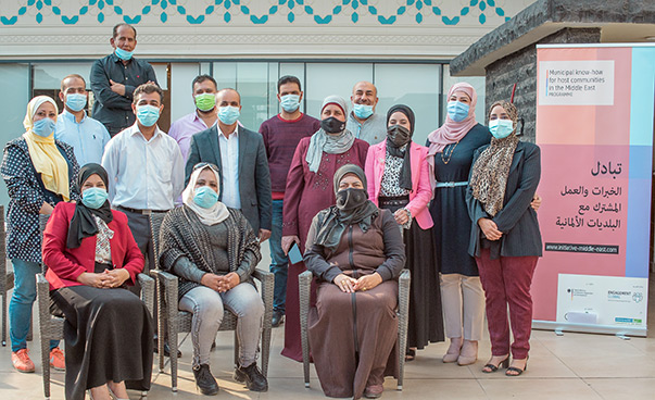 Eight women and seven men, all wearing mouth/nose protection, pose for the camera; to their right is a display wall about the workshop.