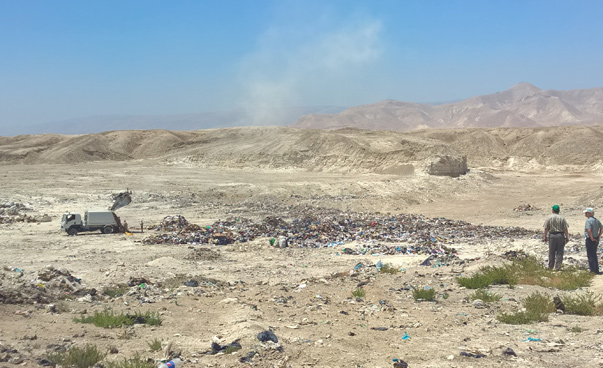 View of an arid valley in Jordan. A garbage truck is parked next to a landfill.