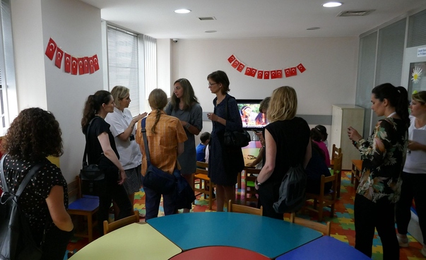 A group of eight persons in a room; some of the women are talking to each other.