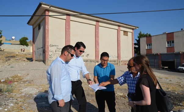 Vier Männer und eine Frau stehen vor einem Gebäude und sehen sich Planungsunterlagen an.