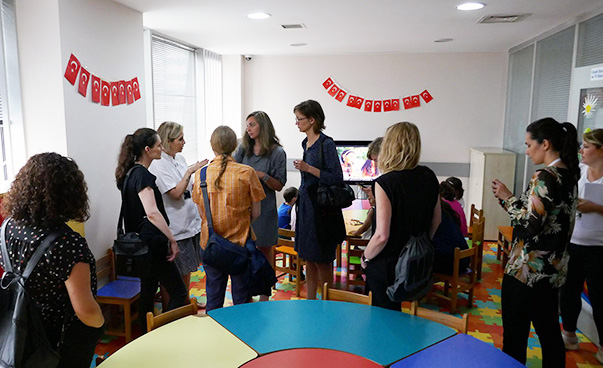 Alternativtext: Eine Gruppe von acht Personen in einem Raum ist zu sehen; einige Frauen sprechen miteinander.
