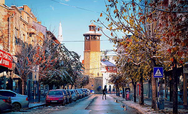Blick auf einen Turm entlang einer von Häusern und Bäumen gesäumten winterlichen Straße.