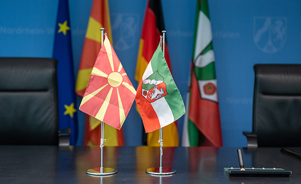 Im Vordergrund sind Tischflaggen von NRW und Nordmazedonien zu sehen; im Hintergrund unscharf zusätzlich die deutsche und europäische Flagge.