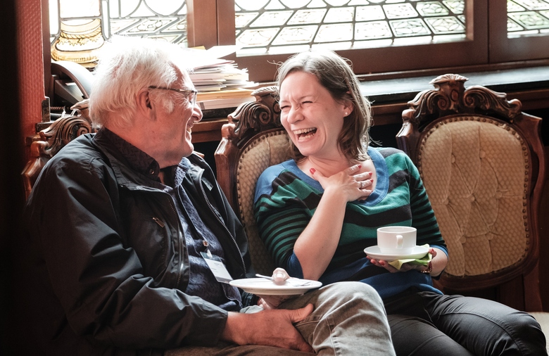 Ein Mann und eine Frau halten Kaffeetassen in der Hand und lachen.