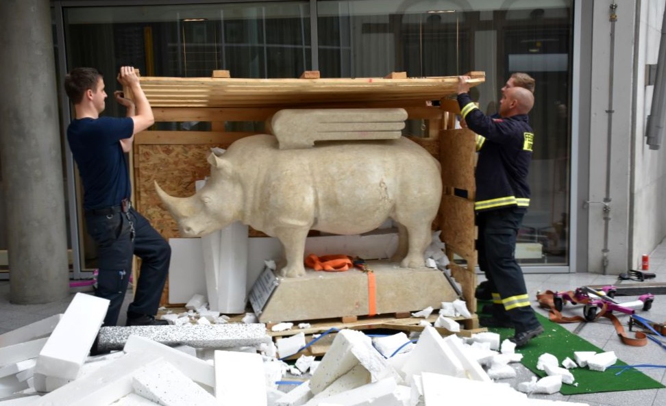 Drei Personen packen ein großes steinerndes Nashorn aus einer Kiste aus.