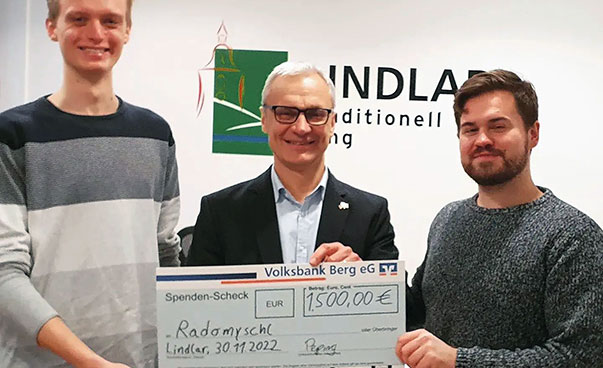 Three smiling men hold up an oversized cheque to the camera.