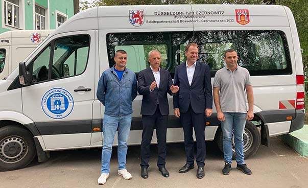 Oberbürgermeister Dr. Stephan Keller und Bürgermeister Roman Klitschuk mit zwei Mitarbeitern der städtischen Betriebe Czernowitz, stehen vor einem Bus, den Düsseldorf der Stadt Czernowitz für Hilfstransporte überlassen hat.