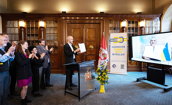 Die beiden Bürgermeister halten jeweils das unterschrieben Dokument in die Luft. Belit Onay in Hannover und Oleksandr Synkevych über Video zugeschaltet in Mykolajiw