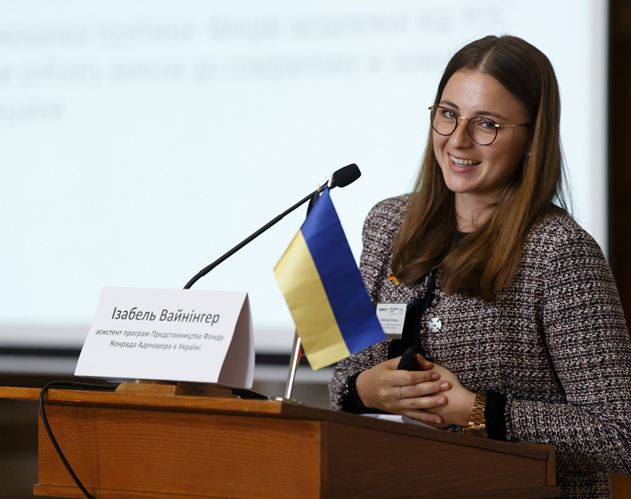 Isabel Weininger spricht lächelnd in ein Mikrofon, an dem eine kleine ukrainische Fahne hängt.