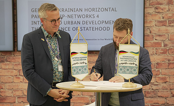 Andreas Wolter, stellvertretender Bürgermeister Kölns und Volodymyr Miller, stellvertretender Bürgermeister von Dnipro stehen vor einem Tisch und unterzeichnen ein Papier, den Letter of Intent.