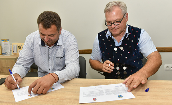 Die beiden Bürgermeister unterschreiben an einem Tisch sitzend ein vor ihnen liegendes Dokument.