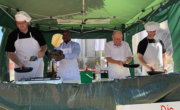 Four people in cooking aprons and caps are standing in a tent, happily handling their pans, among them Vilankulo's mayor and Honorary Consul General Siegfried Lingel.