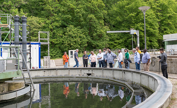 A group of 12 people standing beside a basin of a wastewater treatment plant.