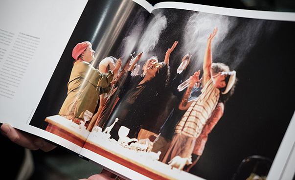 In einem Bild eines aufgeschlagenen Buchs versprühen einige Personen auf einer Bühne Wasser.