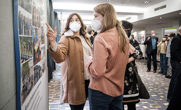 Zwei Frauen stehen vor einer Posterwand und sind im Austausch.