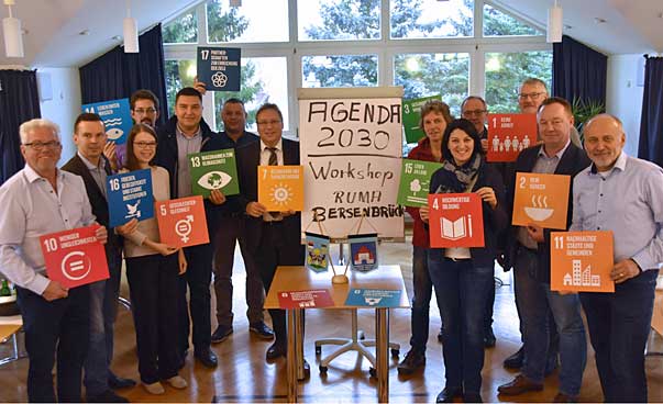 Eine Gruppe lächelt in die Kamera, einige der Personen tragen Schilder mit den Symbolen der 17 nachhaltigen Entwicklungszielen.