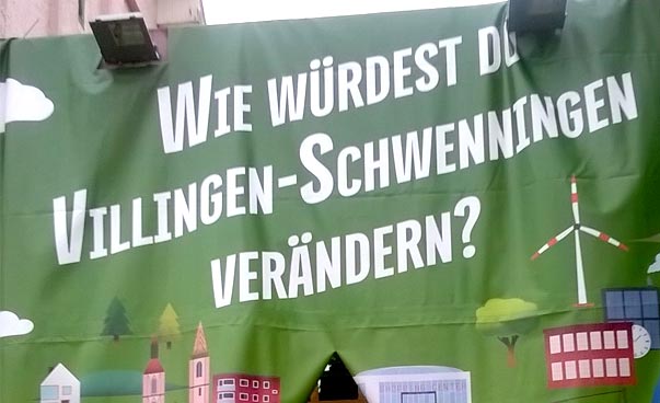 Ein großes Plakat mit der Aufschrift "Wie würdest du Villingen-Schwenningen verändern" bildet den Eingang, durch den man zur Veranstaltung laufen kann.