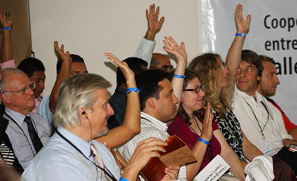 Eine Gruppe von Menschen in einem Saal, einige geben zustimmende Handzeichen.