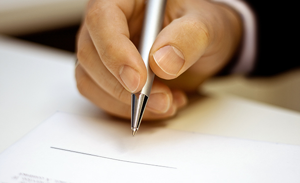 Eine Hand hält einen Stift und schreibt auf einen Block.