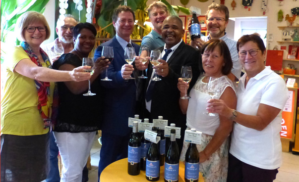 Eine Gruppe von neun Personen, Frauen und Männer aus den Partnerstädten, halten lachend Weingläser in die Höhe. Vor ihnen stehen einige Weinflaschen auf einem Tisch.