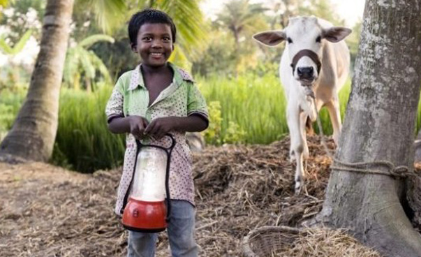 Ein kleiner Junge hält eine Solarlampe in der Hand und lächelt in die Kamera.