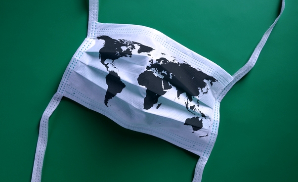 Eine Mund-Nasen-Maske auf grünem Untergrund, auf der eine Weltkarte abgebildet ist