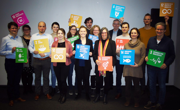 Eine Gruppe von circa 15 Personen hält Schilder mit den Symbolen der nachhaltigen Entwicklungsziele in die Höhe.