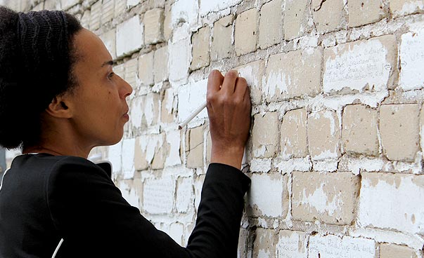 Eine Frau schreibt mit einem Stift an eine Backsteinmauer.