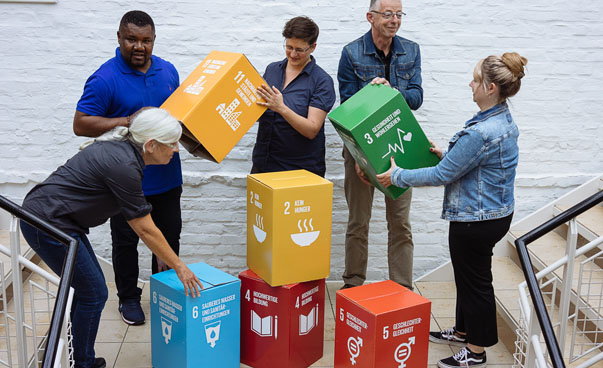 Fünf Personen stapeln große Würfel mit den Symbolen der globalen Nachhaltigkeitsziele übereinander. onen