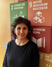 Cristina Aguirre steht vor einer Wand mit einigen globalen Nachhaltigkeitssymbolen