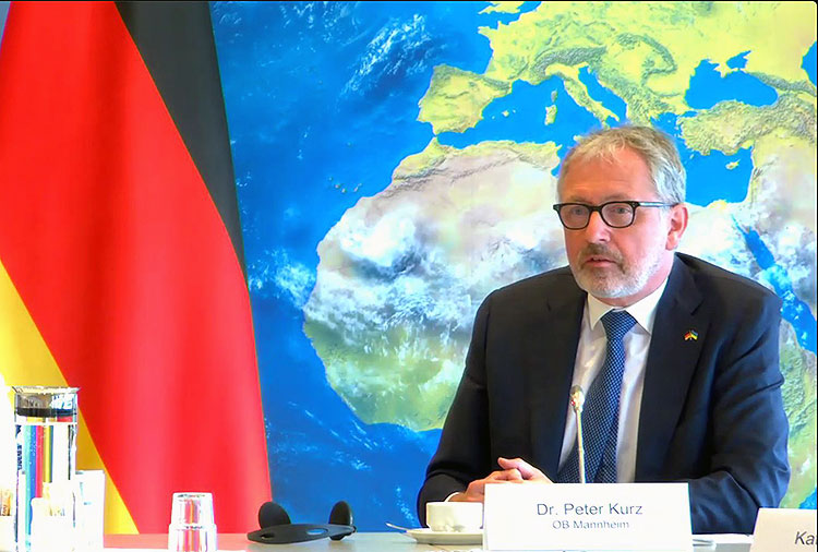 Peter Kurz, Oberbürgermeister von Mannheim, im Vernastaltungsraum. Im Hintergrund eine Deutschlandfahne und eine Weltkarte
