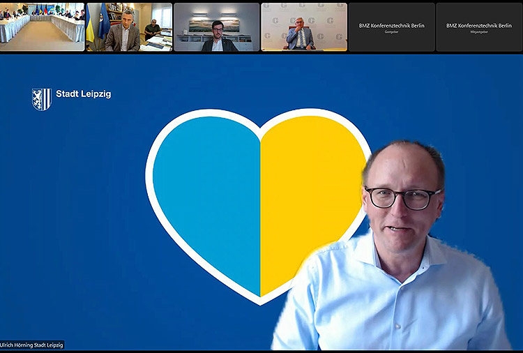 Ulrich Höring per Video zugeschaltet, im Hintergrund ein Herz in den farben der ukrainischen Flagge.